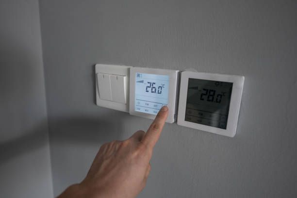 Hand Pointing at A Digital Thermostat Showing 26.0°c on A Gray Wall — Allchin Airconditioning & Refrigeration Electrical in Caloundra, QLD