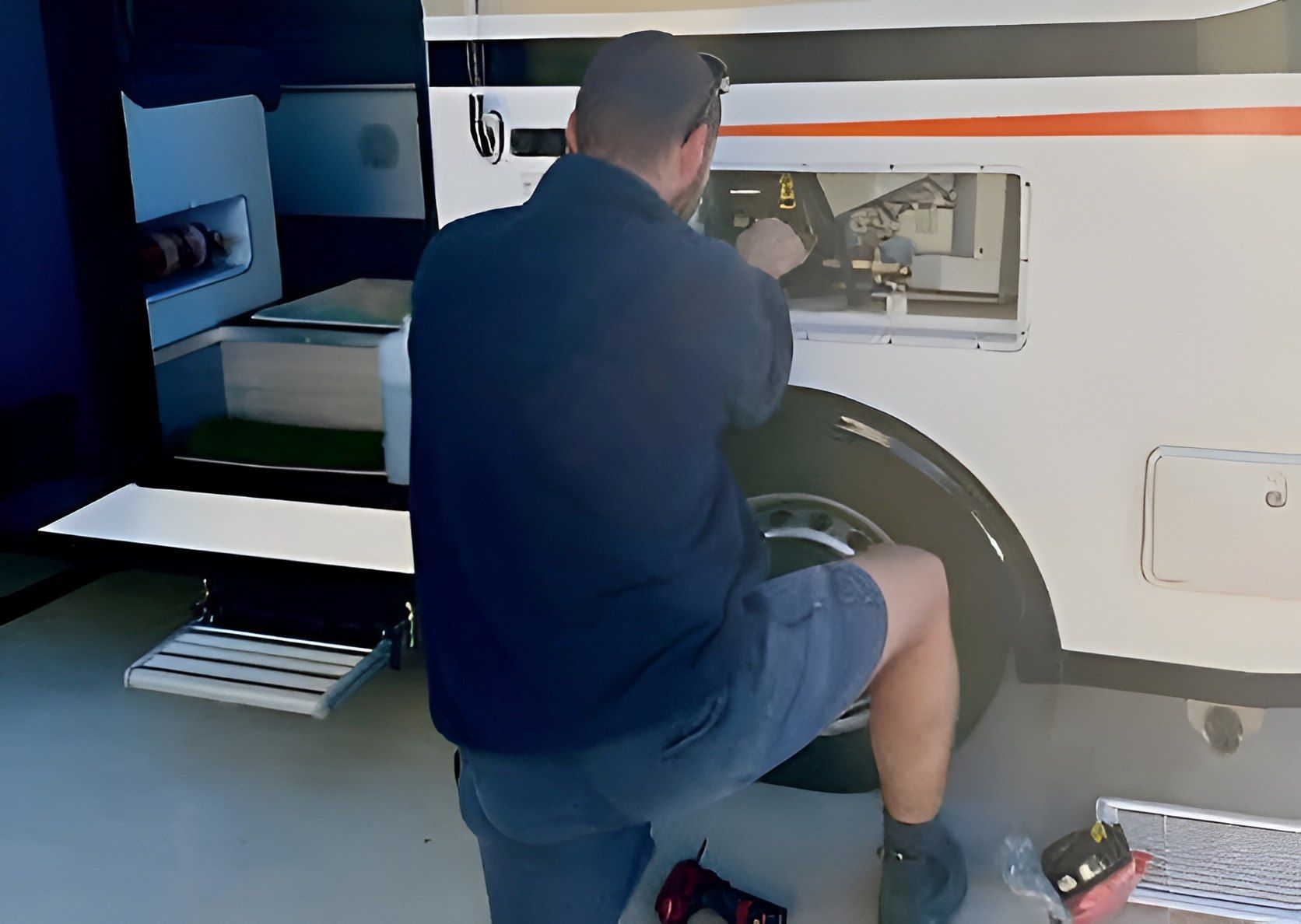 Man Working On The Side Of A White Rv, Crouched Near A Wheel, With Tools Visible — Allchin Airconditioning & Refrigeration Electrical in Caloundra, QLD