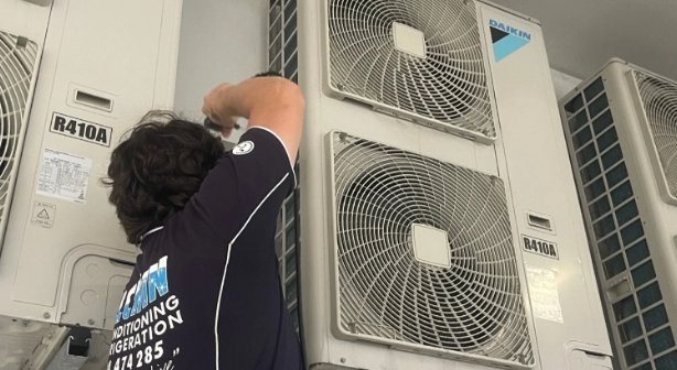 A Man with A Screwdriver Fixing an Air Conditioner — Allchin Airconditioning & Refrigeration Electrical in Caloundra, QLD