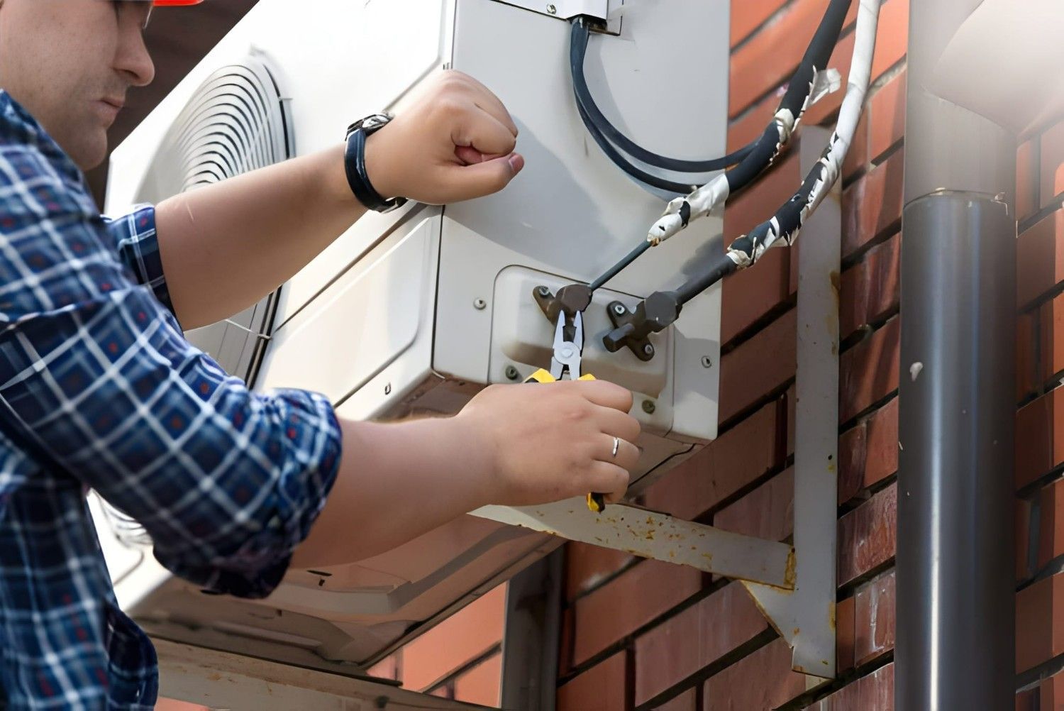 A Person Repairs an Outdoor Air Conditioning Unit on A Brick Wall — Allchin Airconditioning & Refrigeration Electrical in Caloundra, QLD