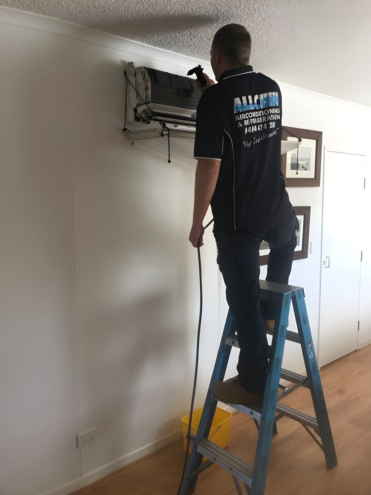Man Cleaning an Air Conditioner on A Ladder — Allchin Airconditioning & Refrigeration Electrical In Caloundra, QLD