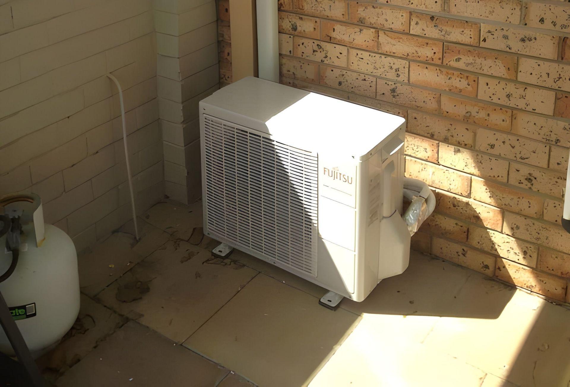 Air Conditioner Unit on A Patio Next to A Brick Wall — Allchin Airconditioning & Refrigeration Electrical in Caloundra, QLD