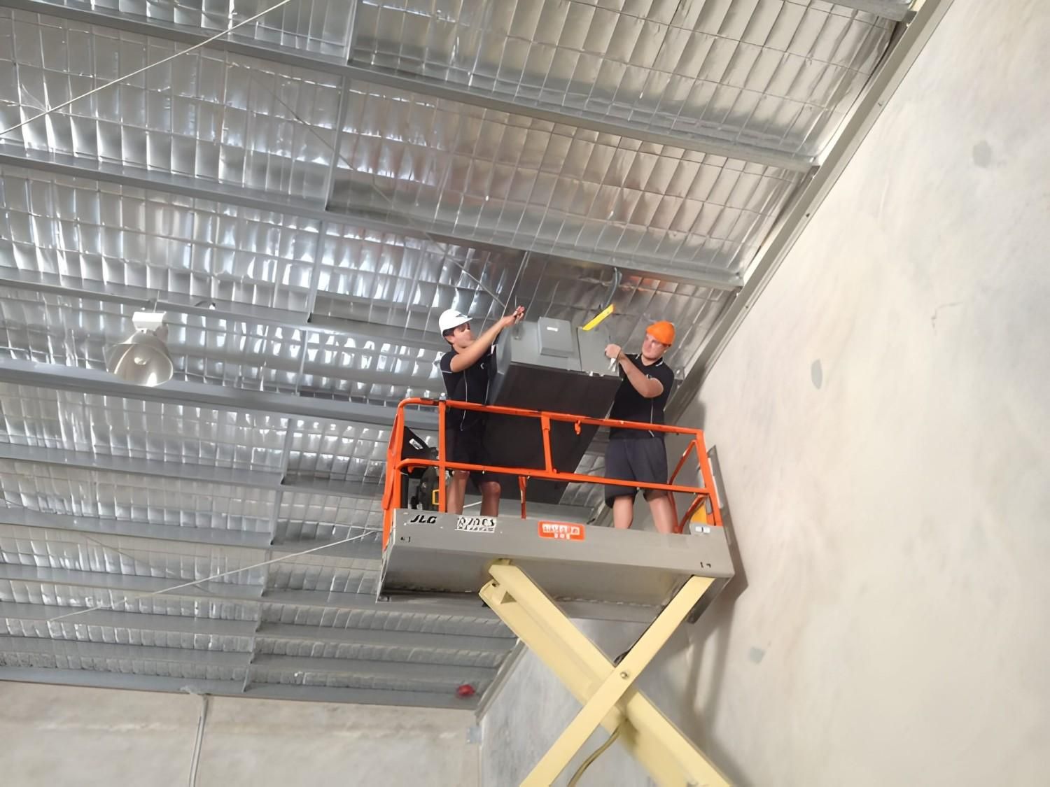 Two Workers Installing Insulation on A Metal Warehouse Ceiling — Allchin Airconditioning & Refrigeration Electrical in Noosa, QLD
