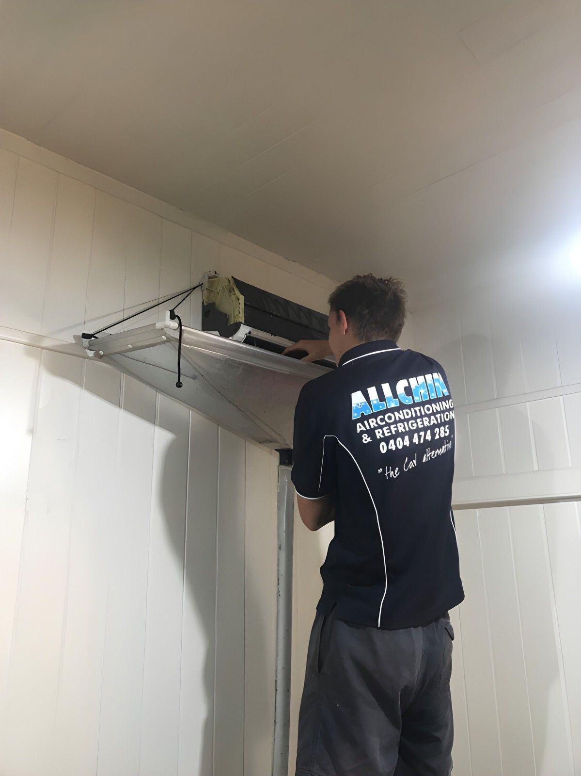 A Man Is Installing Air Conditioner on A White Wall — Allchin Airconditioning & Refrigeration Electrical in Caloundra, QLD