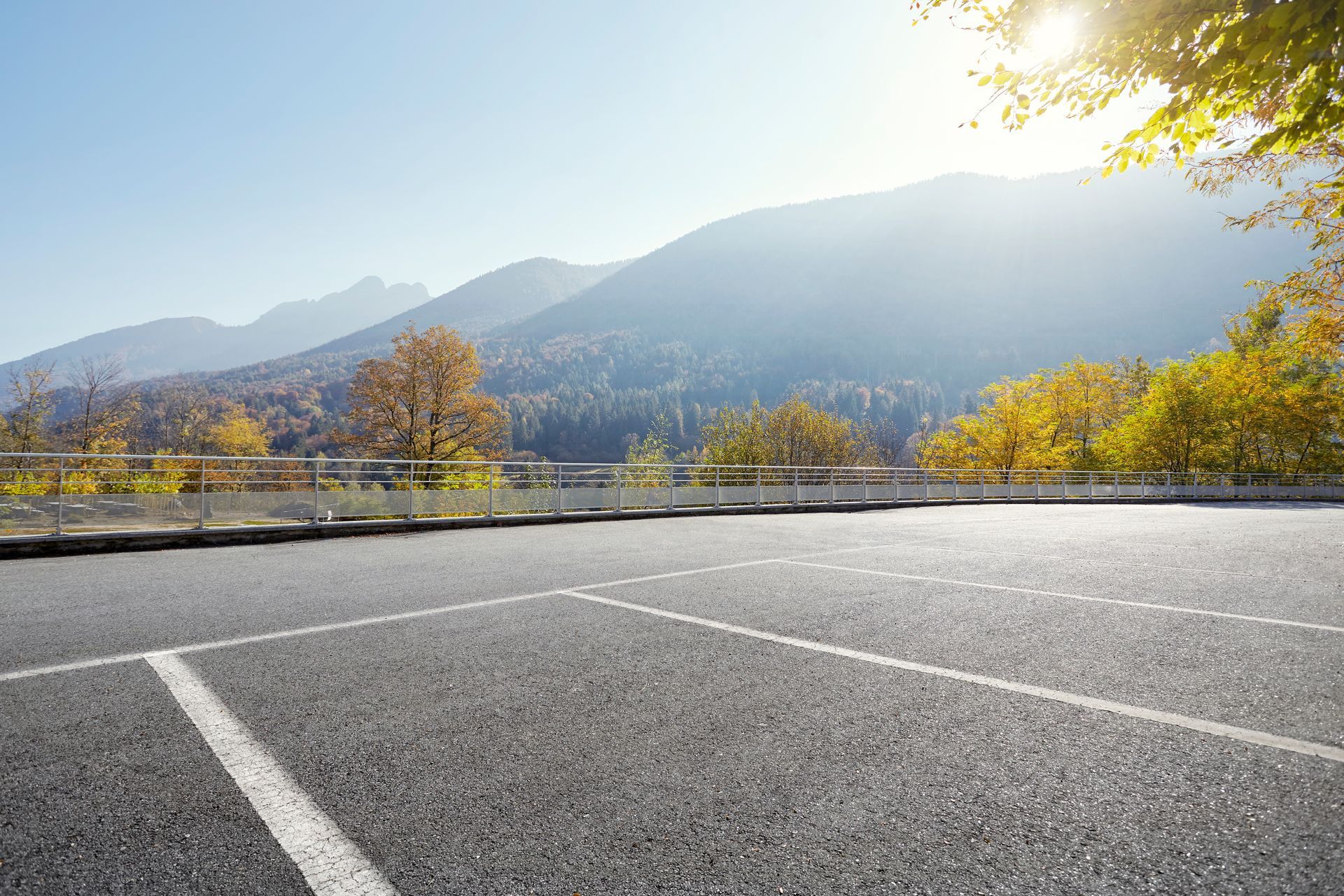 Una strada deserta con le montagne sullo sfondo e il sole che splende attraverso gli alberi.