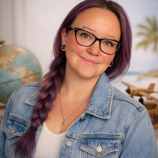 Woman with purple braid and glasses in a denim jacket, smiling in front of a globe and airplane model