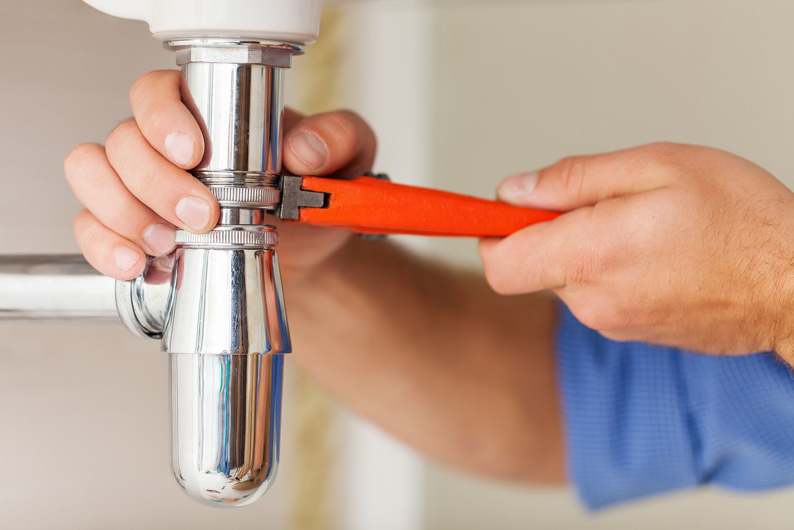 A plumber is fixing a sink pipe with a wrench.
