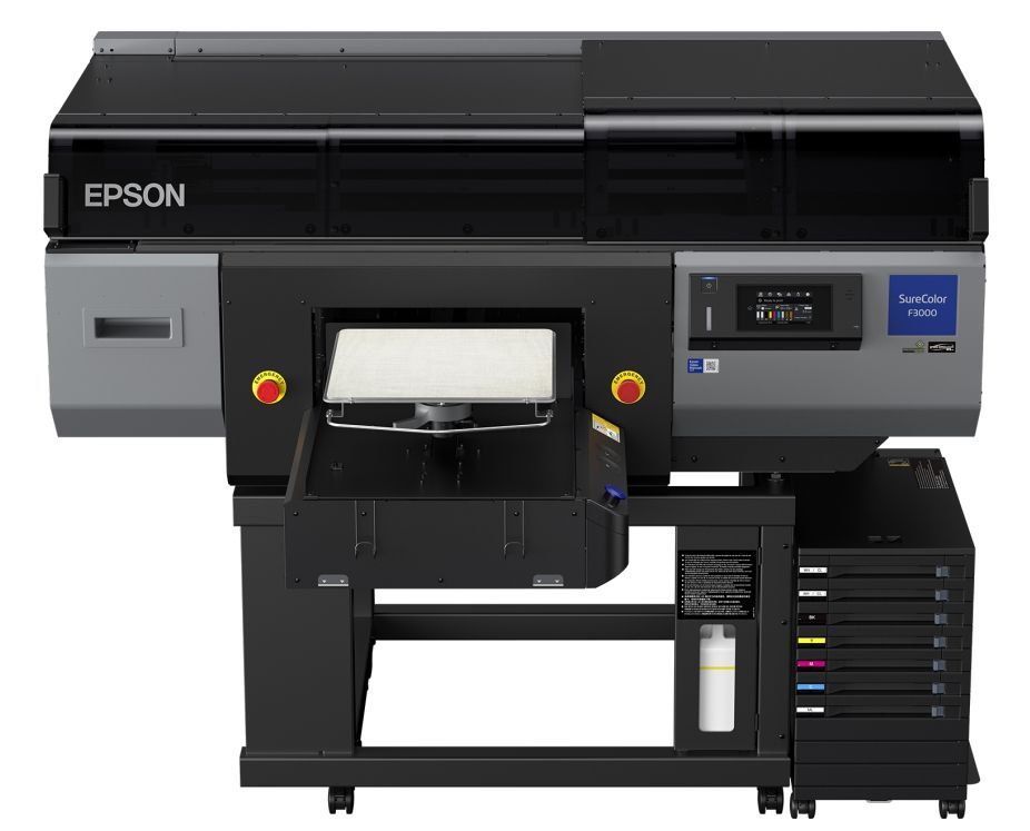 SC-F3000 e o imprimantă direct-to-garment (DTG) foarte rezistentă, gândită pentru cei care au nevoie de productivitate mare. E o soluție DTG flexibilă care îi ajută pe utilizatori să răspundă rapid la comenzi. Imprimanta oferă o precizie ridicată, așa că firmele pot livra rapid, chiar și atunci când e vorba de modele complicate pe tot felul de articole din bumbac, fie ele deschise sau închise la culoare. Pe lângă toate astea, costurile de utilizare rămân reduse, ceea ce o face potrivită pentru companii de dimensiuni medii sau mari din industria de îmbrăcăminte și tricouri.
Când vine vorba de productivitate, Epson a adăugat câteva funcții care fac munca mai ușoară. De exemplu, imprimanta ajustează automat spațiul dintre plăci, detectând singură cât de groasă e suprafața pe care lucrezi, așa că poți schimba rapid între diferite tipuri de haine. Sistemul de cerneală vrac de 1,5 litri face ca reîncărcarea să fie simplă și rapidă. Mai mult, ai la dispoziție software-ul Epson Production Monitor, care îți arată în timp real ce se întâmplă cu imprimanta, fie pe telefon, fie pe calculator. În plus, cele două capete de imprimare PrecisionCore MicroTFP, care pot fi schimbate chiar de către utilizator, ajută la menținerea imprimantei în stare bună de funcționare.
Tehnologia din spatele acestei imprimante simplifică procesul de producție și crește calitatea finală. Picăturile de cerneală sunt plasate precis, așa că imprimarea iese mereu clară și uniformă. Sistemul de verificare automată a duzelor (NVT) se asigură că totul funcționează cum trebuie și ajustează din mers dacă apare vreo problemă, ca să nu ai surprize neplăcute.
Fiabilitatea nu lipsește nici ea. Imprimanta are mai multe funcții de auto-întreținere, cum ar fi un nou kit de ștergere, un filtru de praf mai mare și curățarea automată a capacului, toate gândite să reducă la minimum intervențiile manuale.
Și dacă te preocupă mediul, e bine de știut că cernelurile folosite respectă standardul global pentru textile organice (GOTS) și se încadrează în cerințele Oeko-Tex 100 pentru textile ecologice de calitate. Practic, poți să produci haine sigure și prietenoase cu natura, fără bătăi de cap.