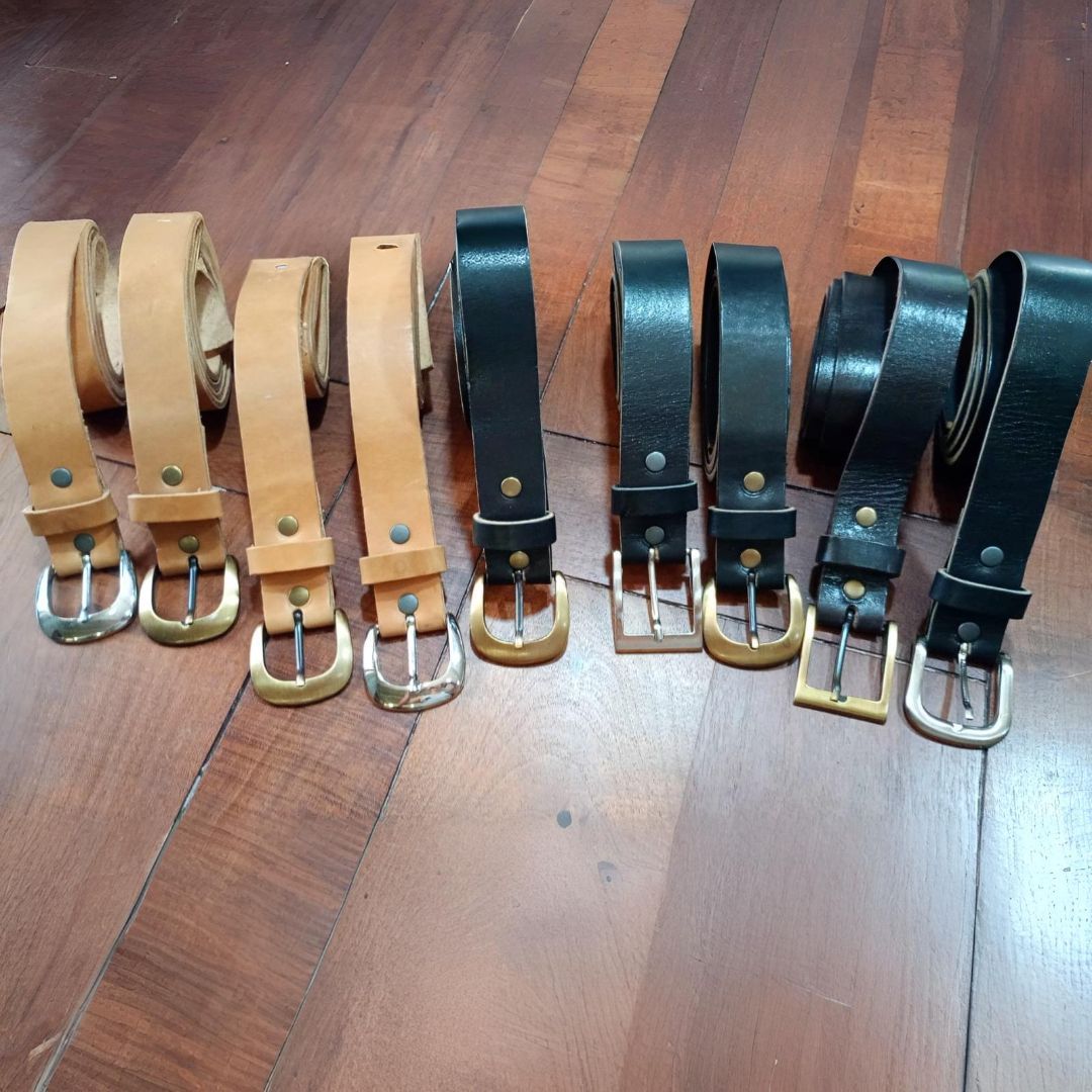 Siete cinturones de cuero de varios colores colocados sobre una superficie de madera.