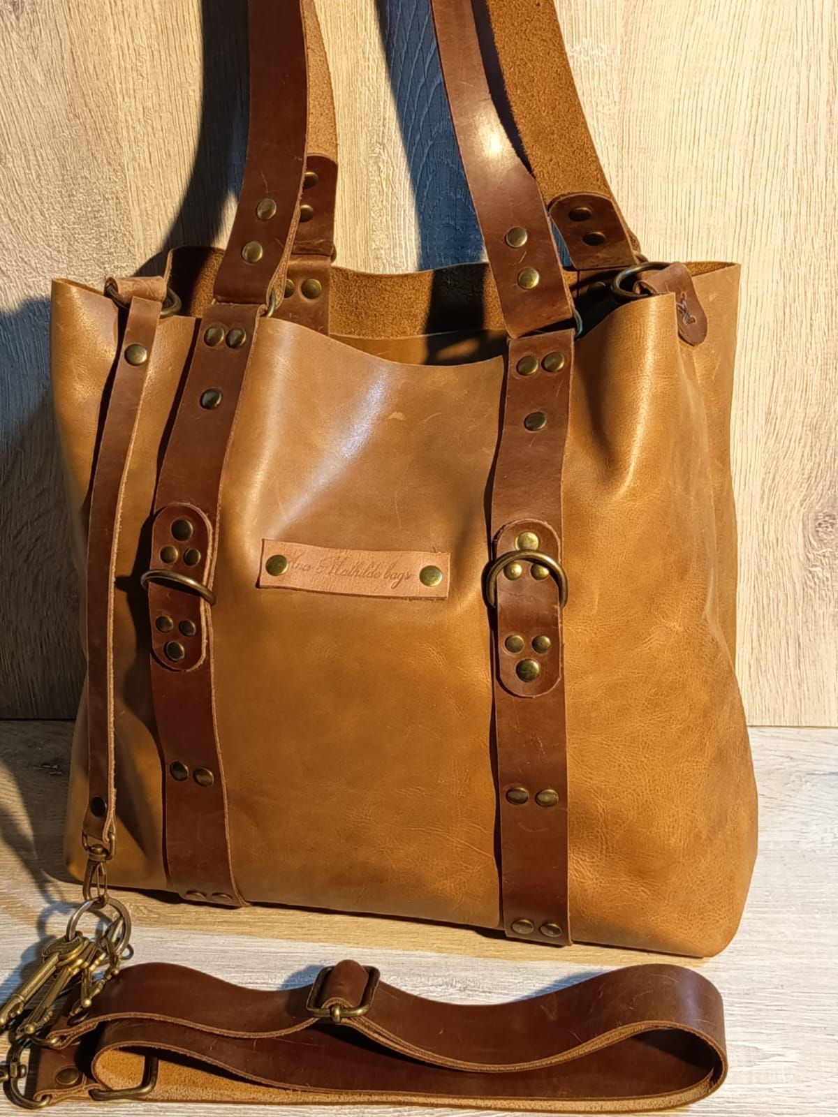 Bolso tote de piel color tostado con correas marrones, hebillas y correa de hombro extraíble.