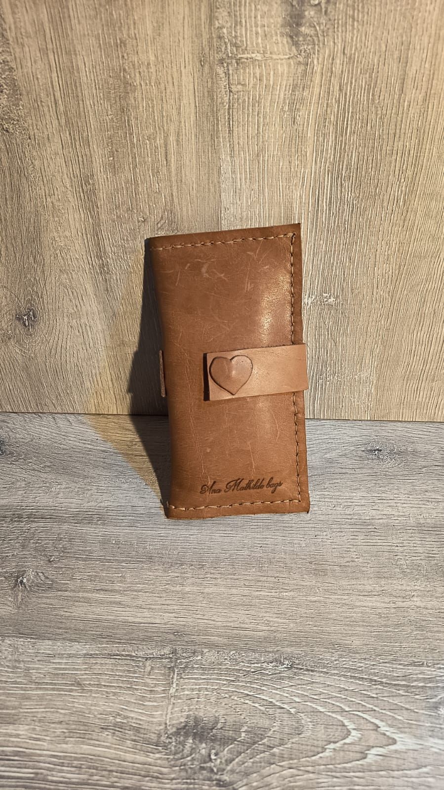 Cartera de piel marrón con cierre en forma de corazón sobre superficie de madera.
