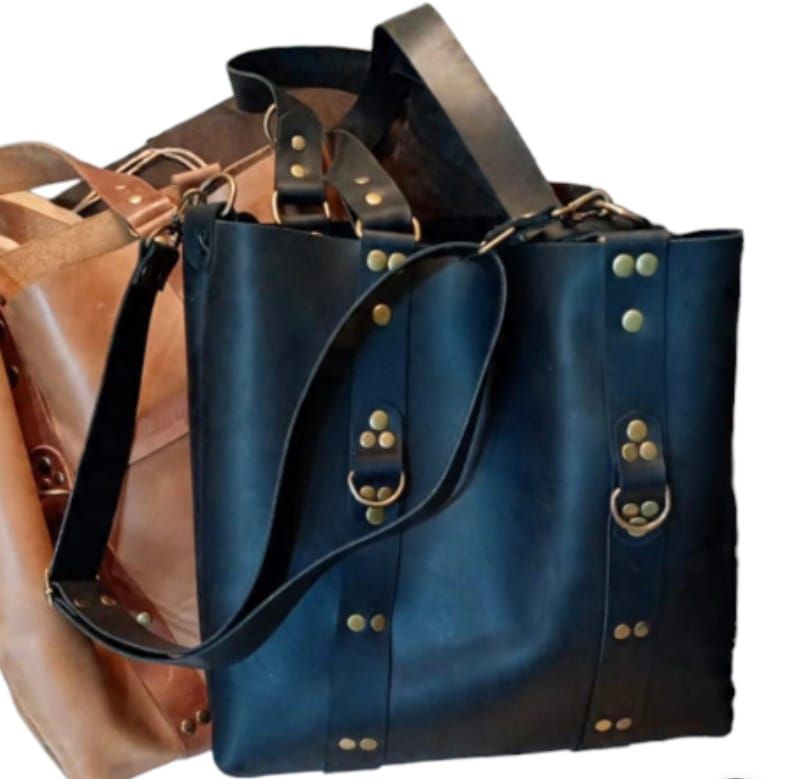 Bolso de mano de piel negra con correa para el hombro y herrajes de latón, junto a un bolso de piel color tostado.