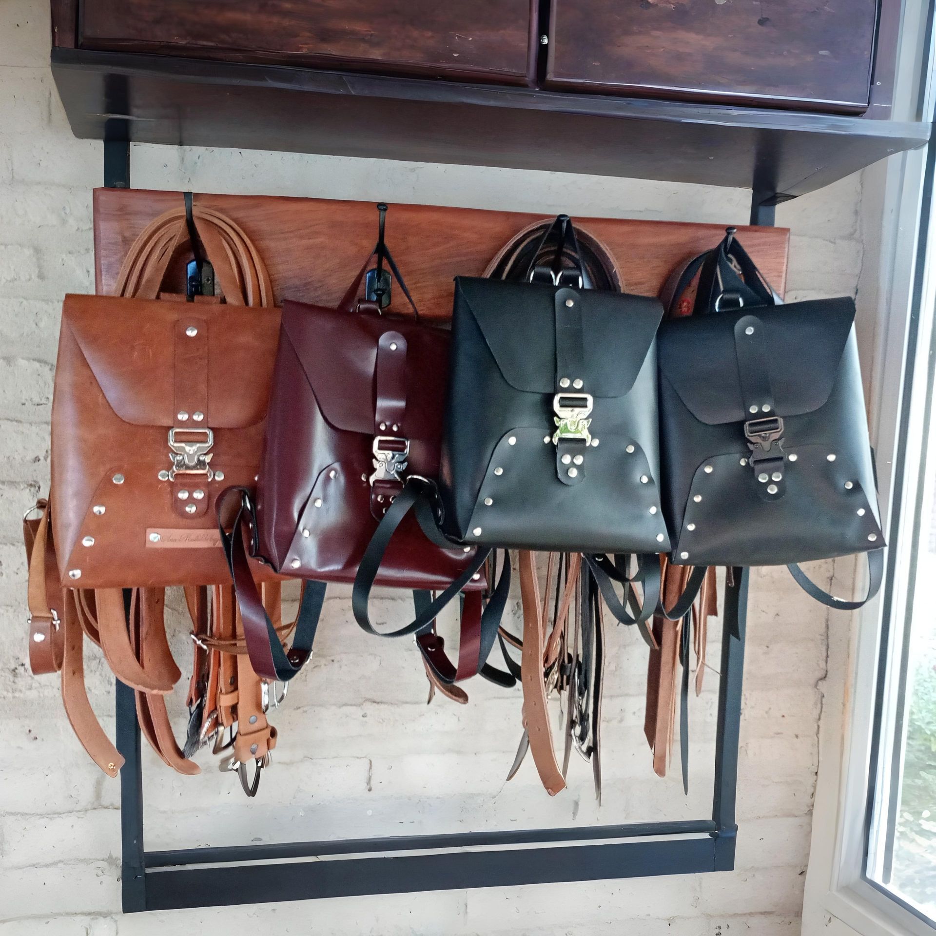 Cuatro mochilas de cuero colgadas en un estante de metal negro, en varios colores marrón y negro.