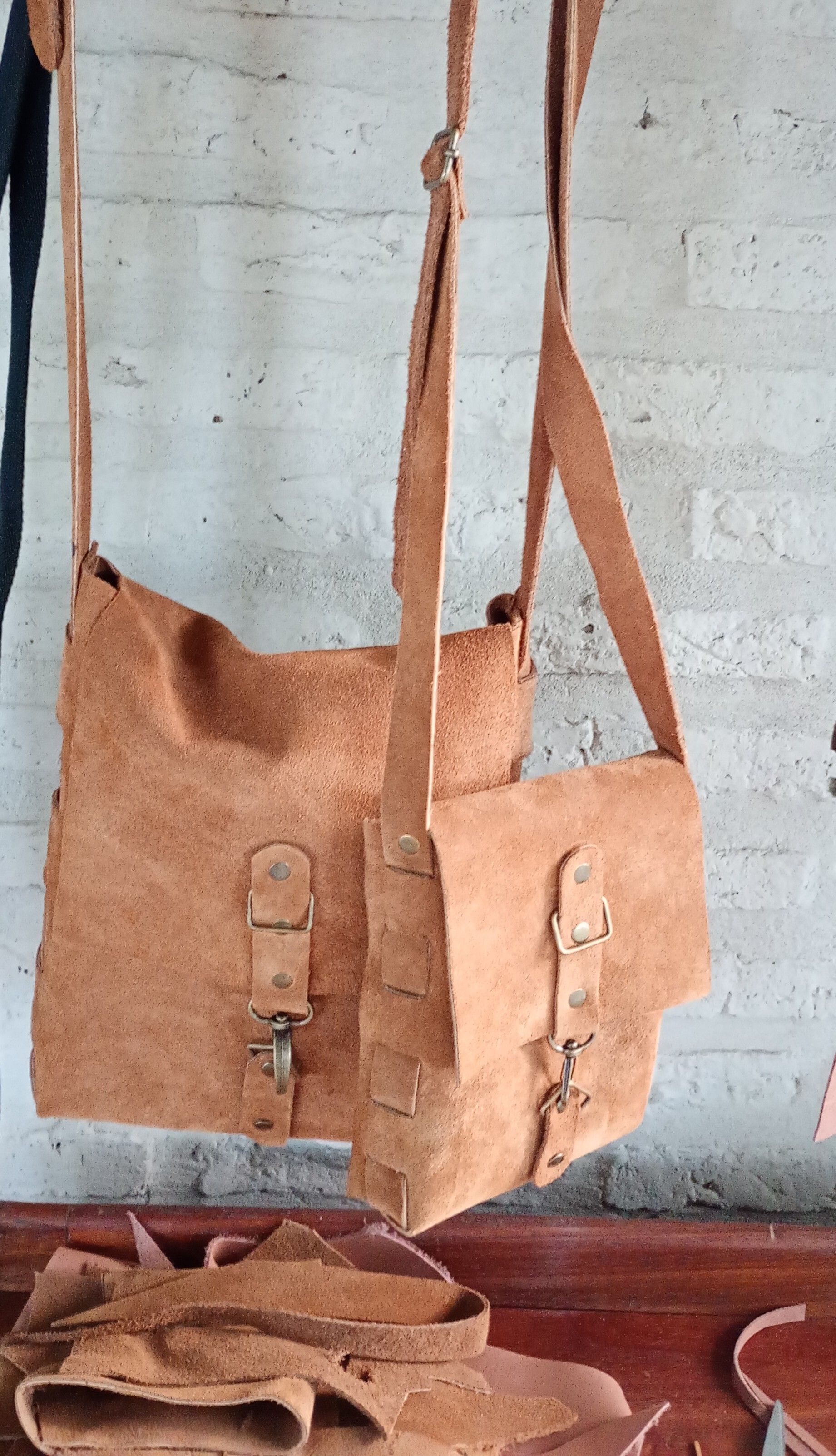 Dos bolsos de hombro de cuero color canela colgados sobre una pared texturizada.