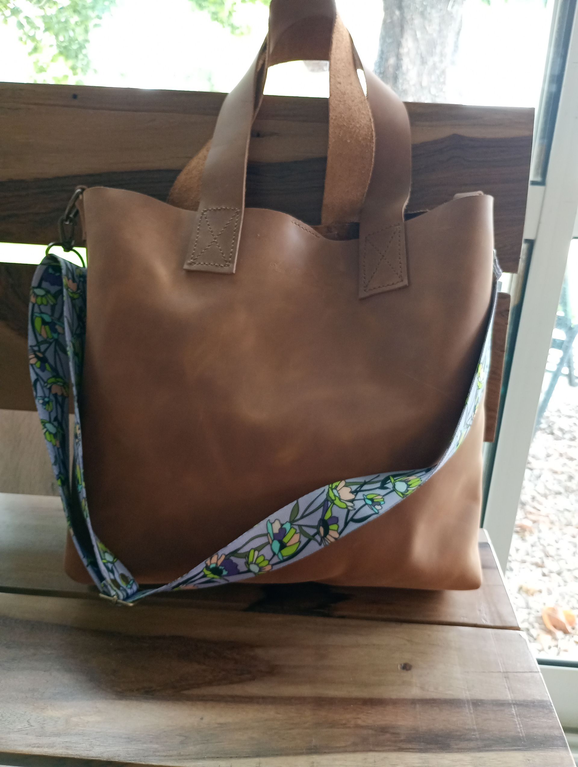 Bolso tote de piel marrón con correa estampada, colocado sobre una superficie de madera.