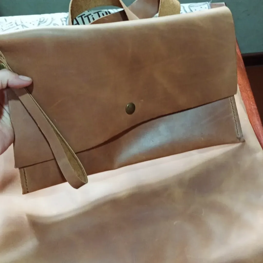 Bolso de mano de piel color canela con correa para la muñeca, que se sostiene con la mano de una persona.