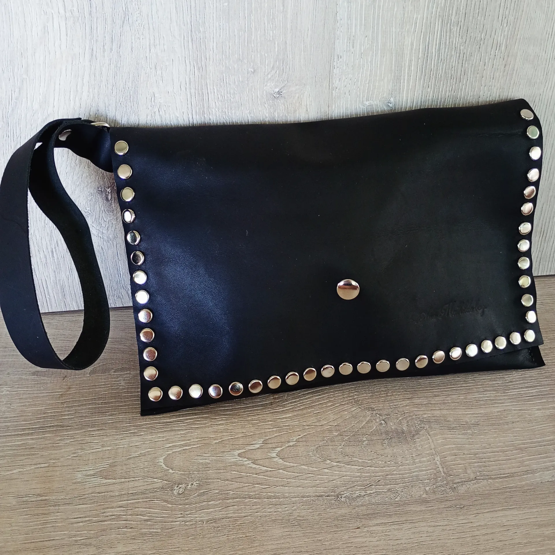 Clutch de piel negra con tachuelas plateadas, correa negra.