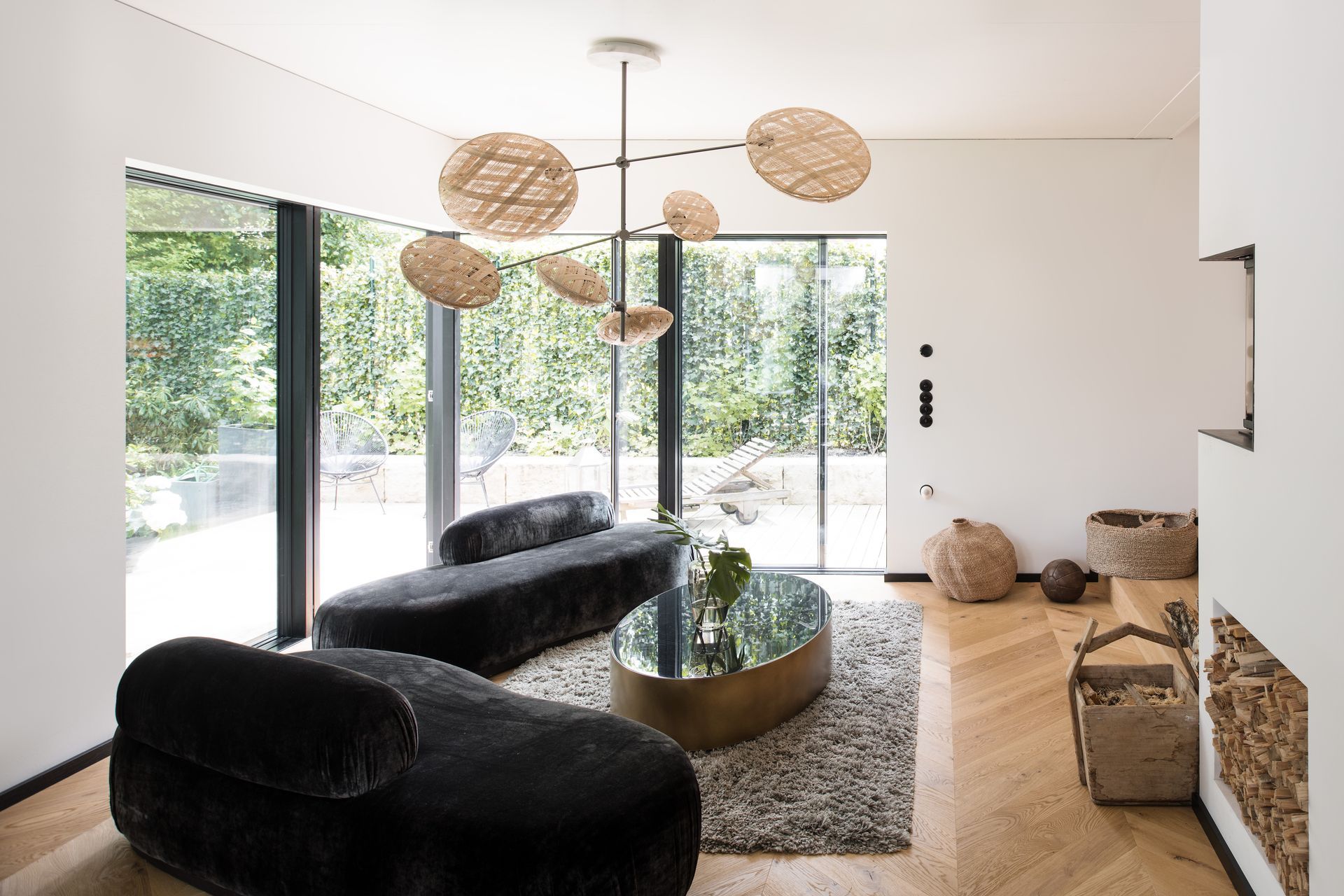 Living room with black velvet sofas, round woven pendant lights, and large windows.