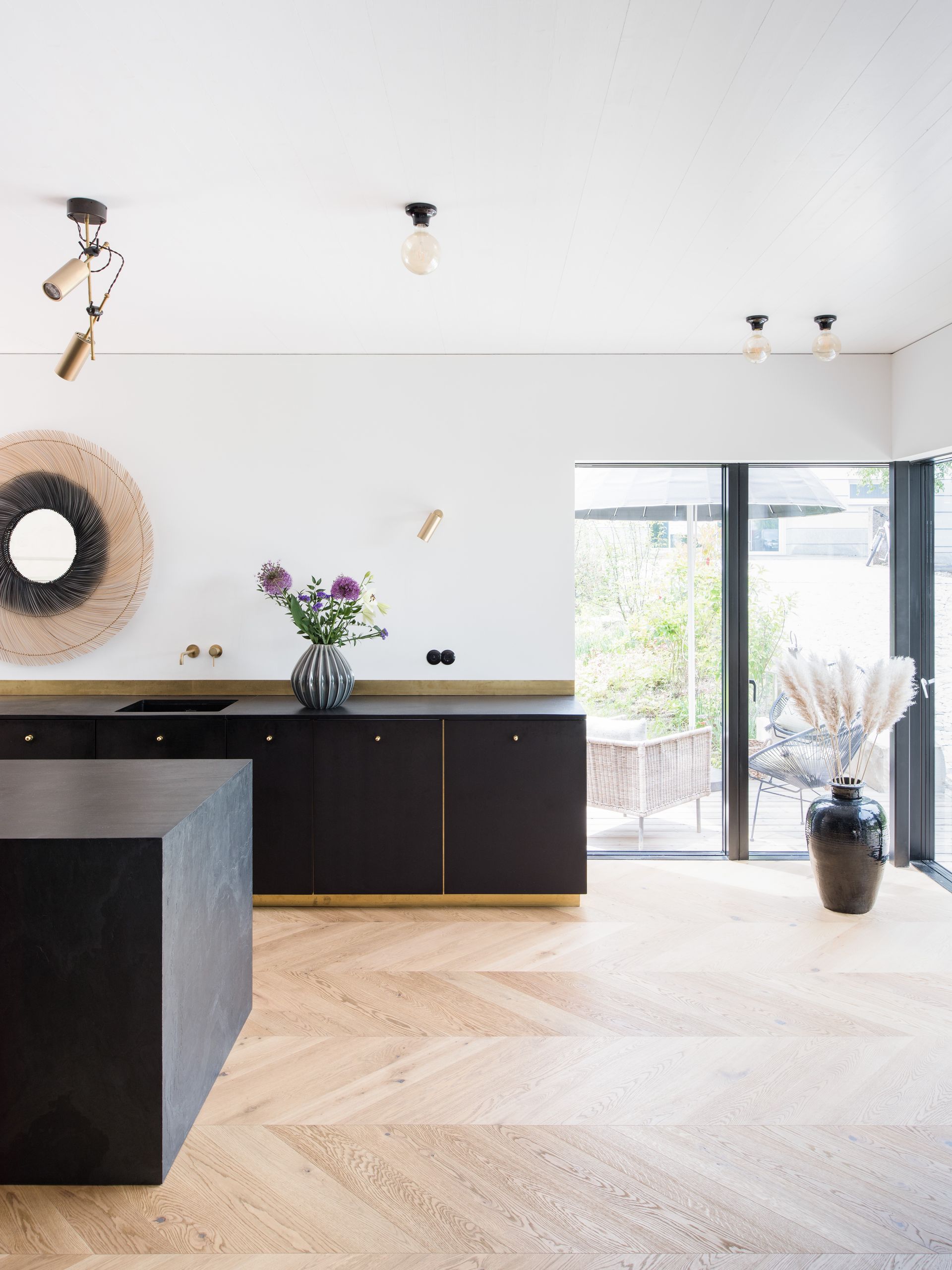 Modern black kitchen with gold accents, herringbone floors, and a glass door.