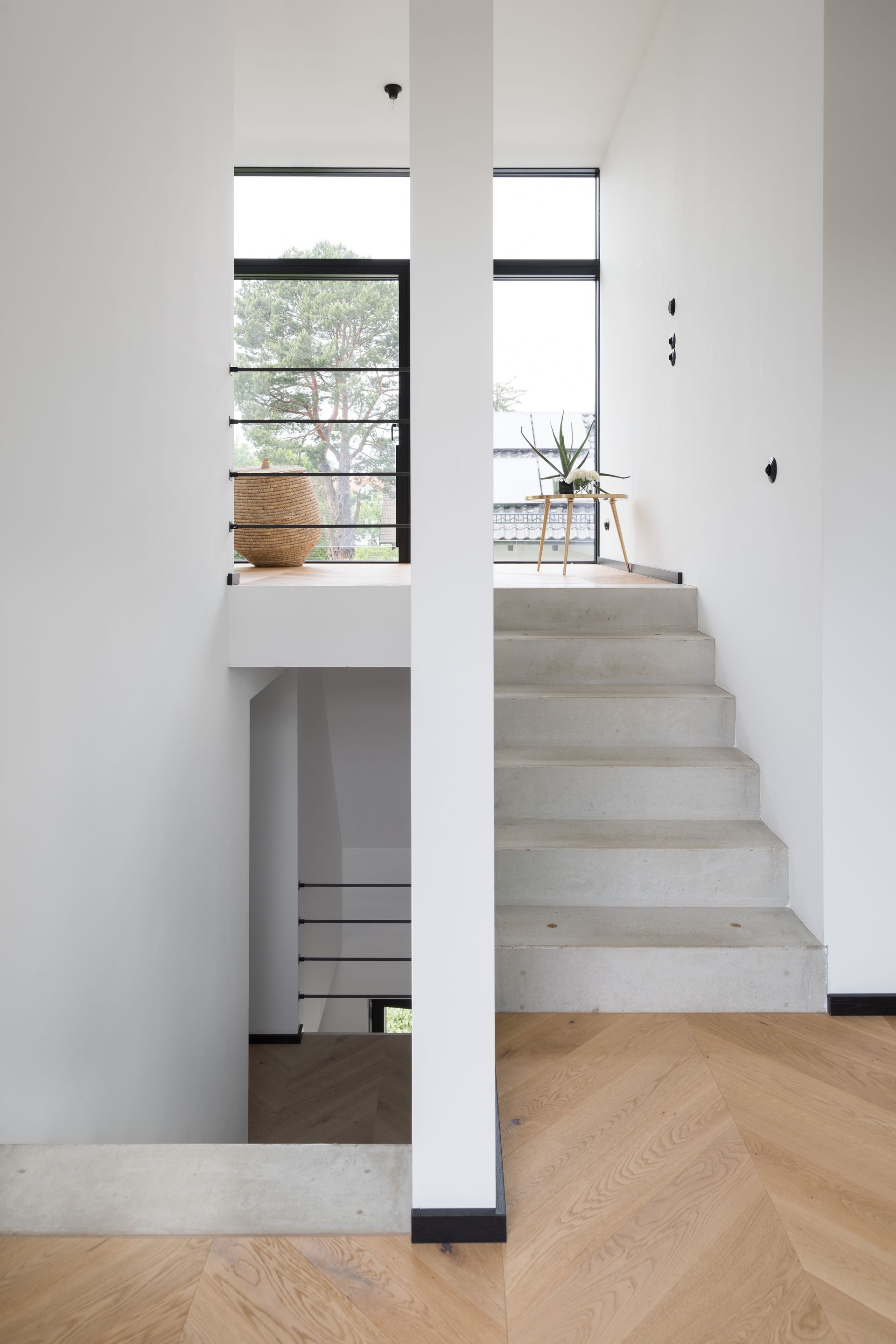 Concrete staircase with white walls, black accents, and wood flooring. A balcony and large window are visible.