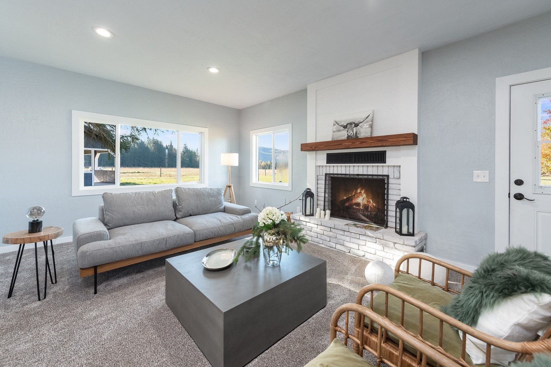 Cozy living room with fireplace, gray sofa, and modern coffee table. Light blue walls and large windows.