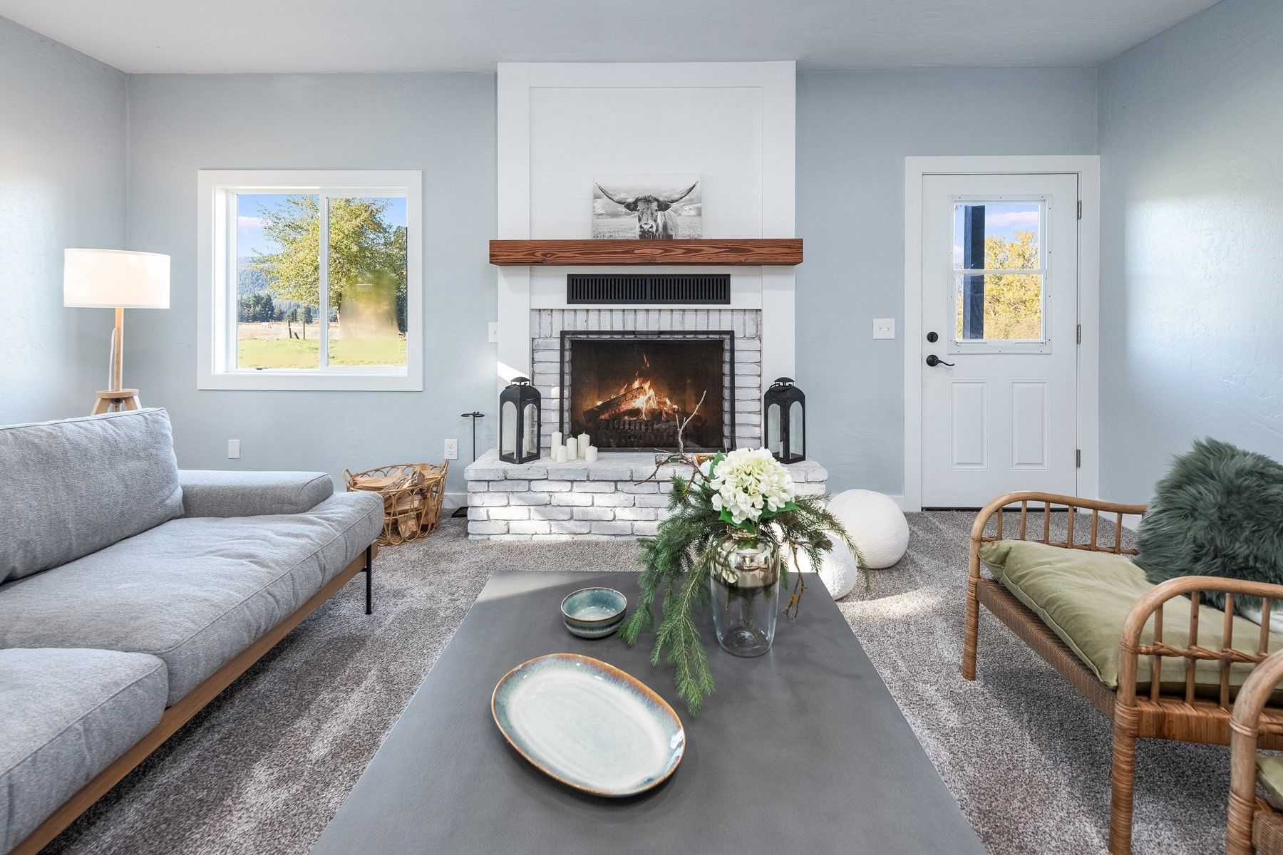 Living room with fireplace, gray sofa, coffee table with floral arrangement, and a doorway.