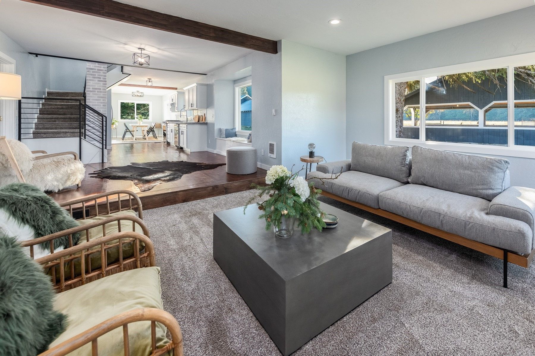 Living room with gray sofa, wicker chairs, a dark wood coffee table, and a large window.