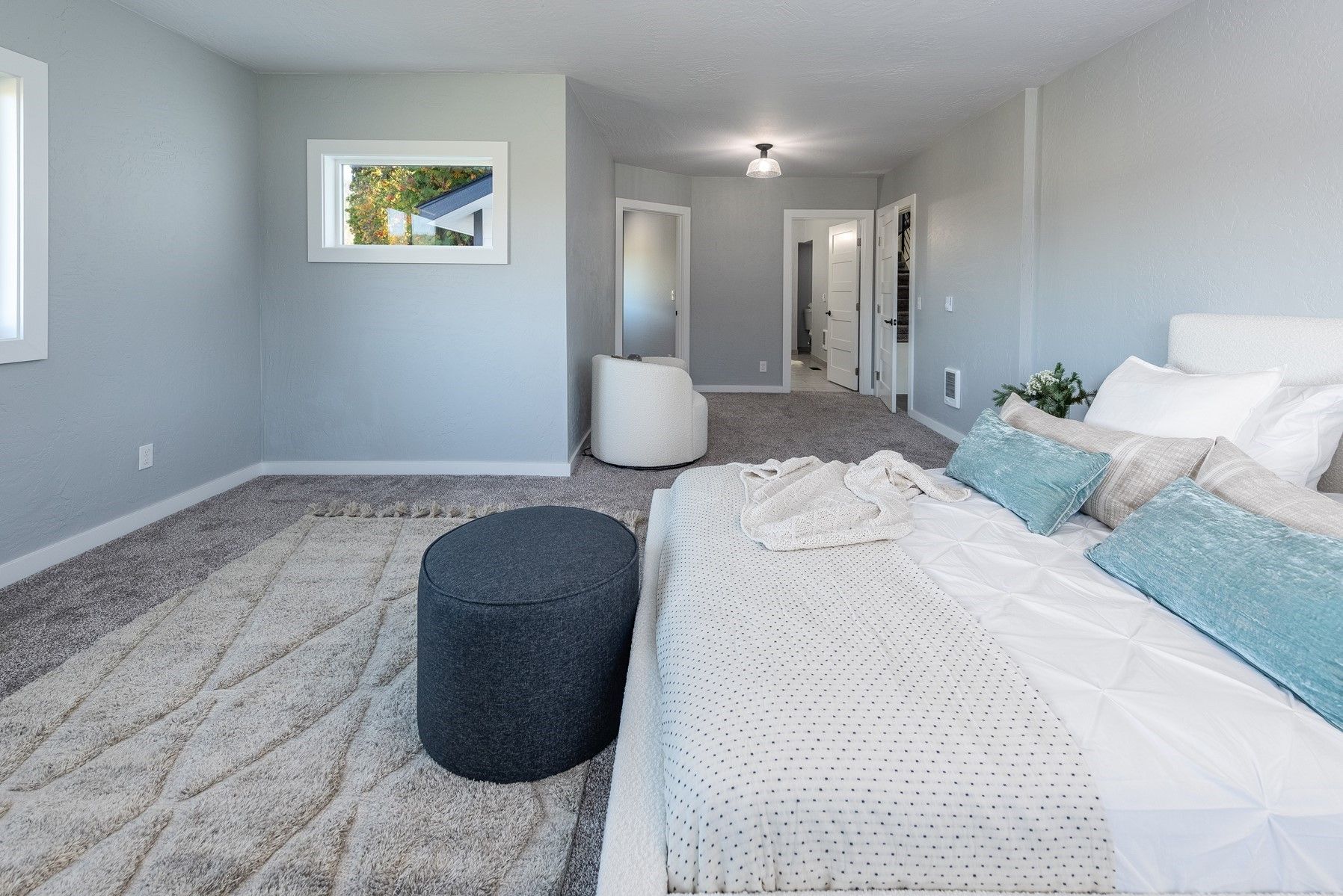 Spacious bedroom with gray walls, shaggy rug, and large bed with turquoise pillows.