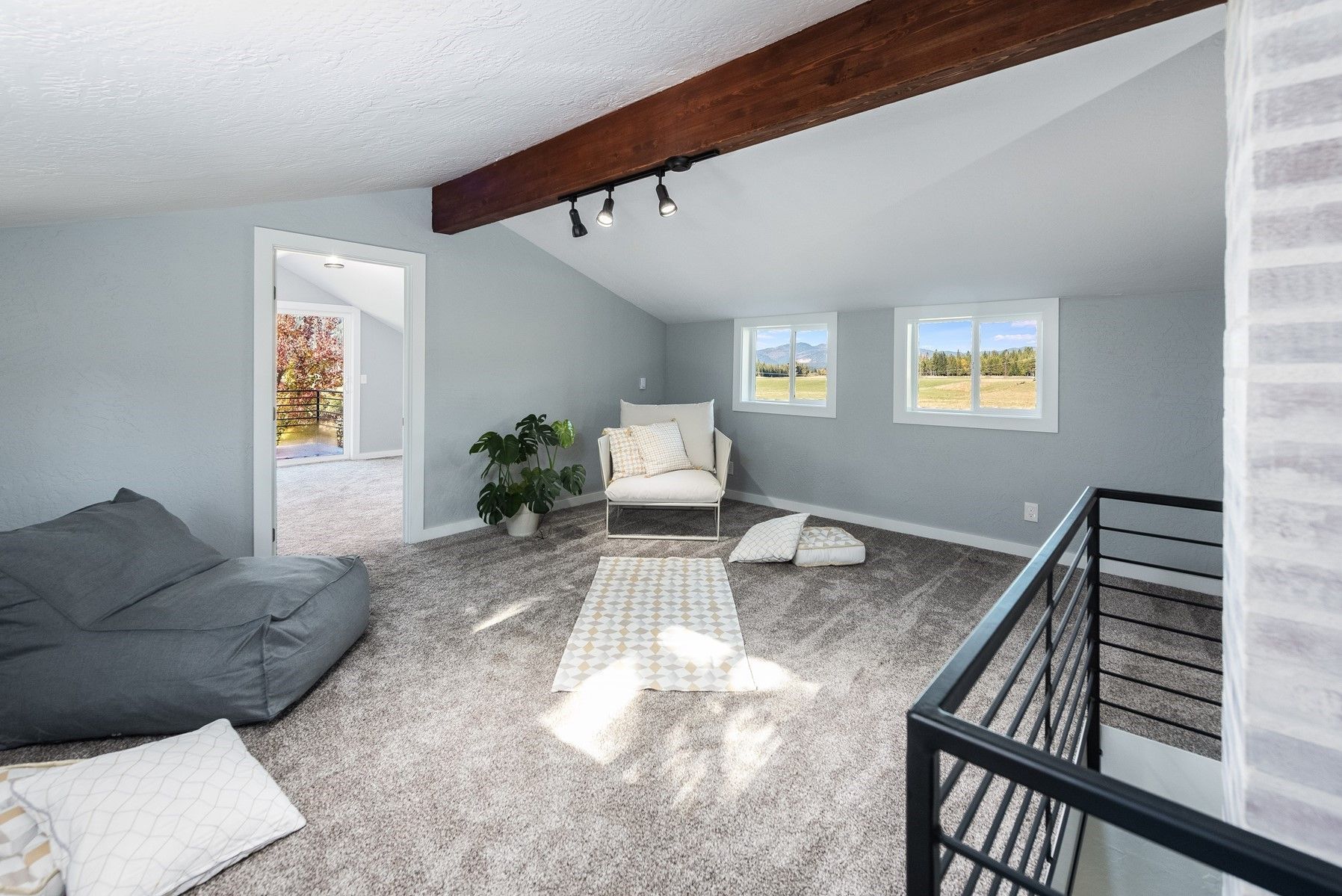 Loft room with angled ceiling, neutral gray walls, exposed wood beam, seating area, small windows, and brick accent wall.