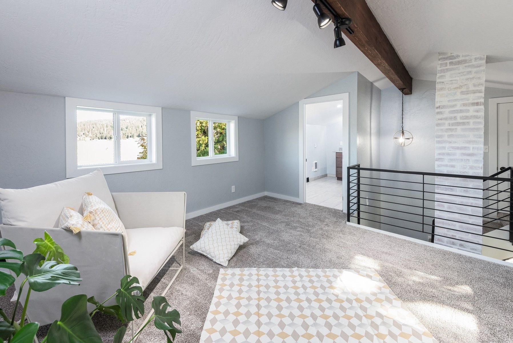 Cozy, light-filled living room with white sofa, gray carpet, brick accent wall, and wooden beam.