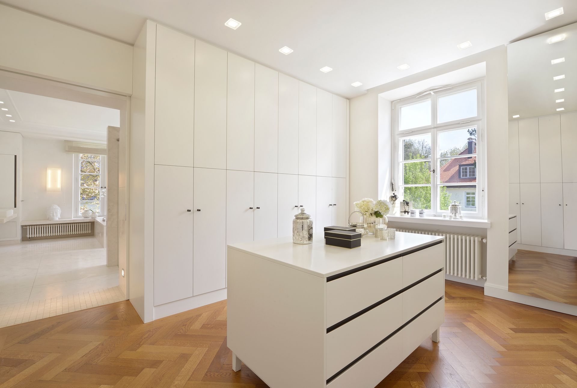White dressing room with storage cabinets, dresser, hardwood floors, and window.