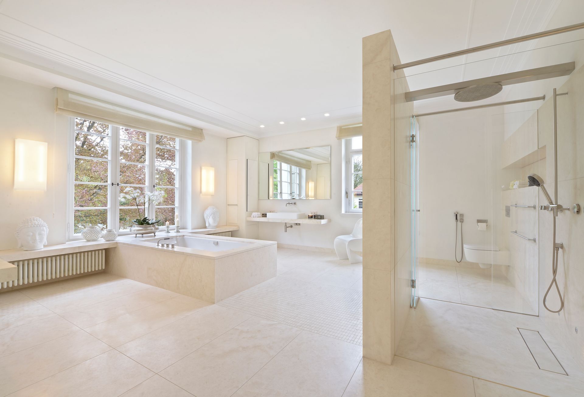 Spacious, all-white bathroom with a large bathtub, walk-in shower, and natural light from large windows.