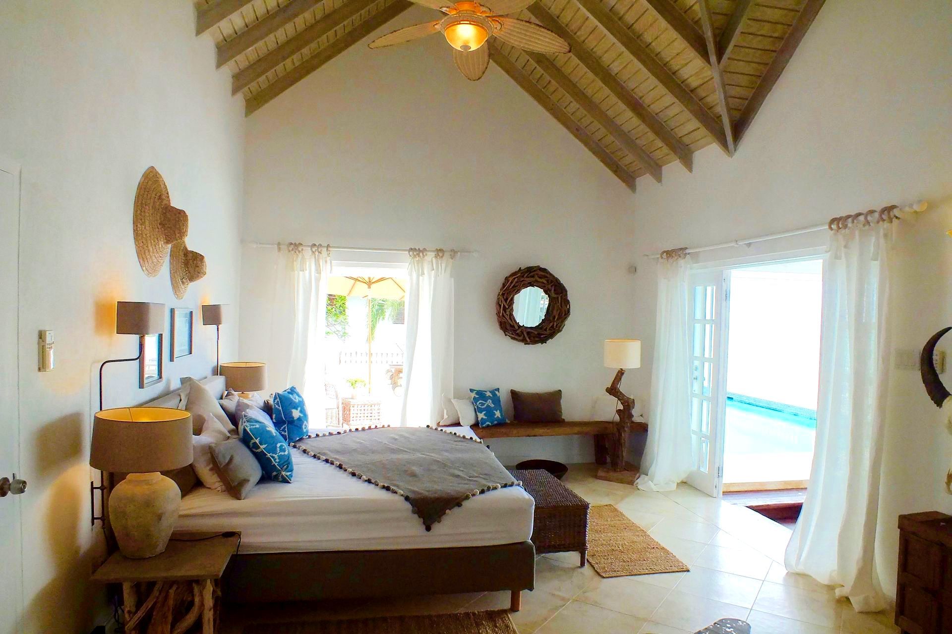 Bedroom with a high ceiling, bed, doors leading to a pool, and decor in neutral tones.