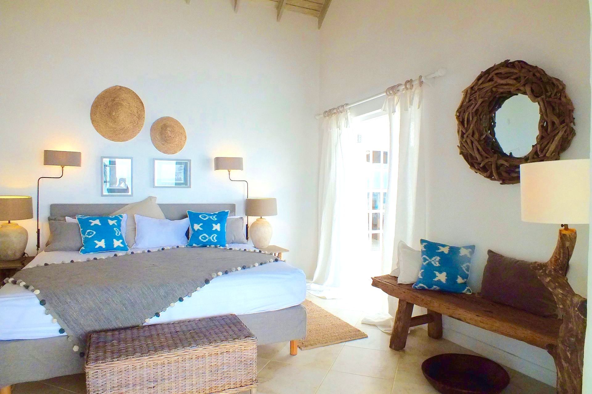 Bedroom with white walls, large bed, wood bench, and woven decor.