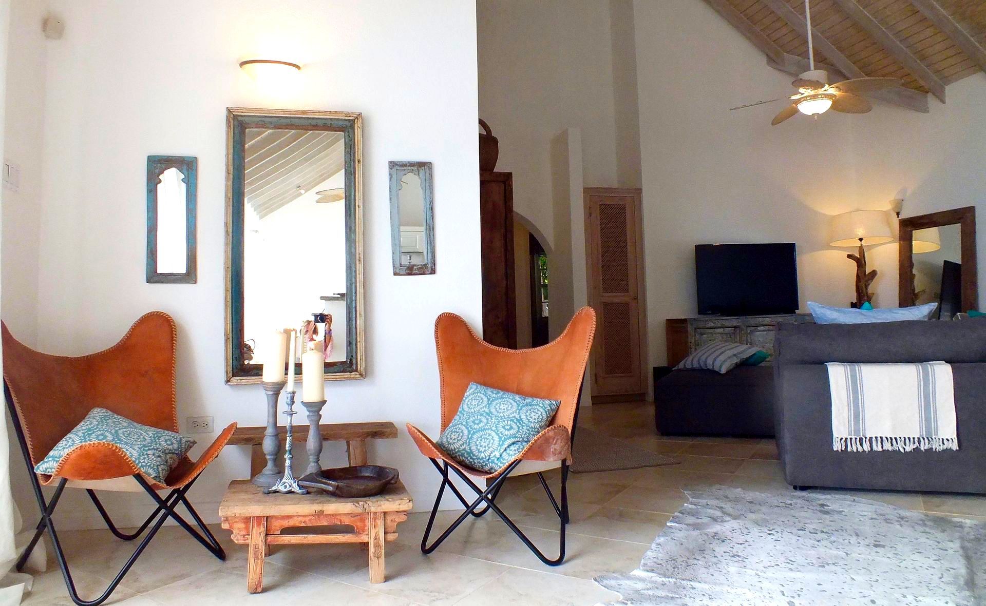 Living room with butterfly chairs, a small table, a mirror, and a couch. White walls and a textured ceiling.
