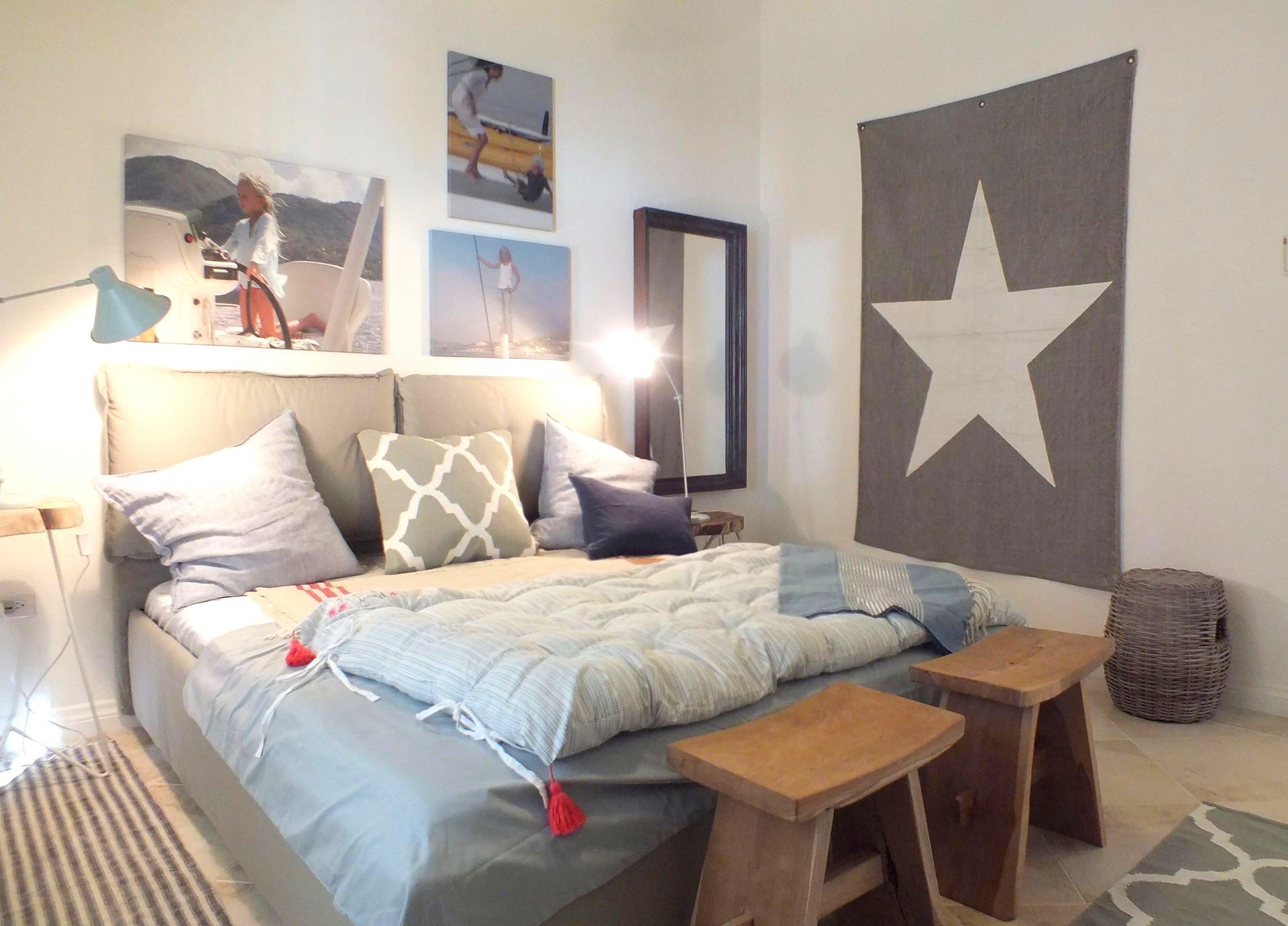 Bedroom with bed, art, stools, rug, and star tapestry. Soft colors and cozy atmosphere.