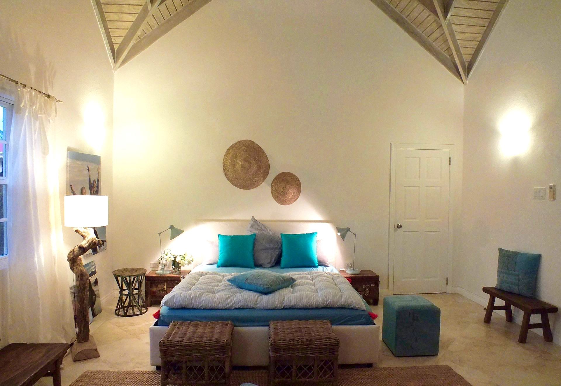 Bedroom with white walls, vaulted ceiling, bed with blue pillows, and natural decor.