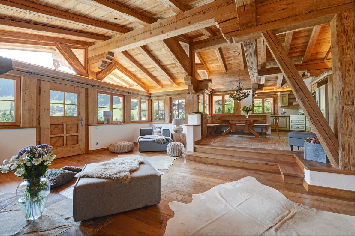 Cozy wooden interior with exposed beams, windows, and a dining area, featuring a living space with seating.