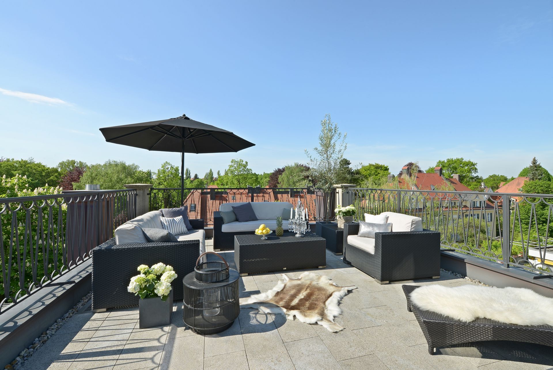 Rooftop patio with black outdoor furniture, umbrella, and a fur rug under a blue sky.