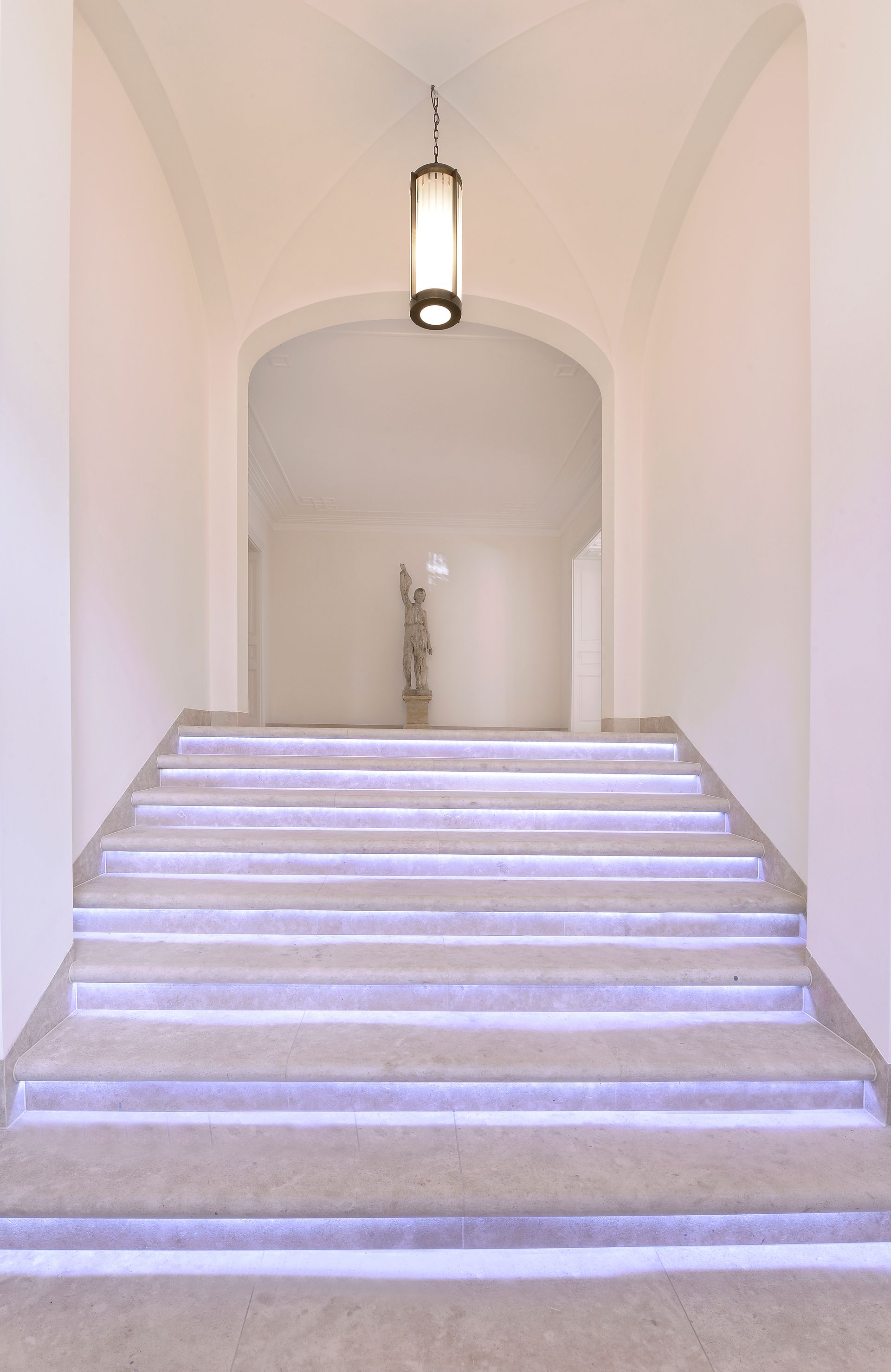 Staircase leading to a bright hallway, illuminated steps, pendant light overhead.