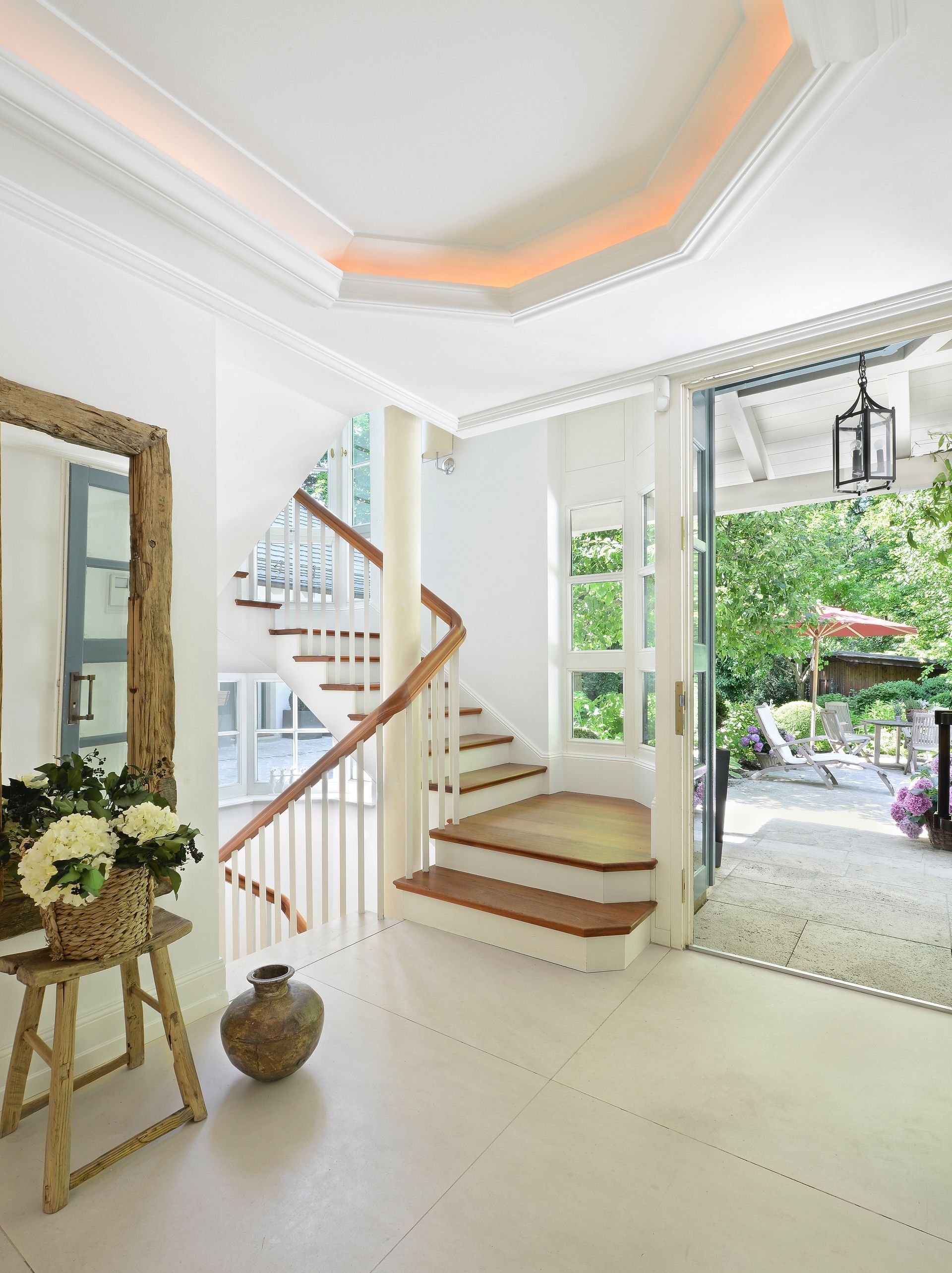 Bright white foyer with a curved staircase, open door to a patio, and decorative mirror.