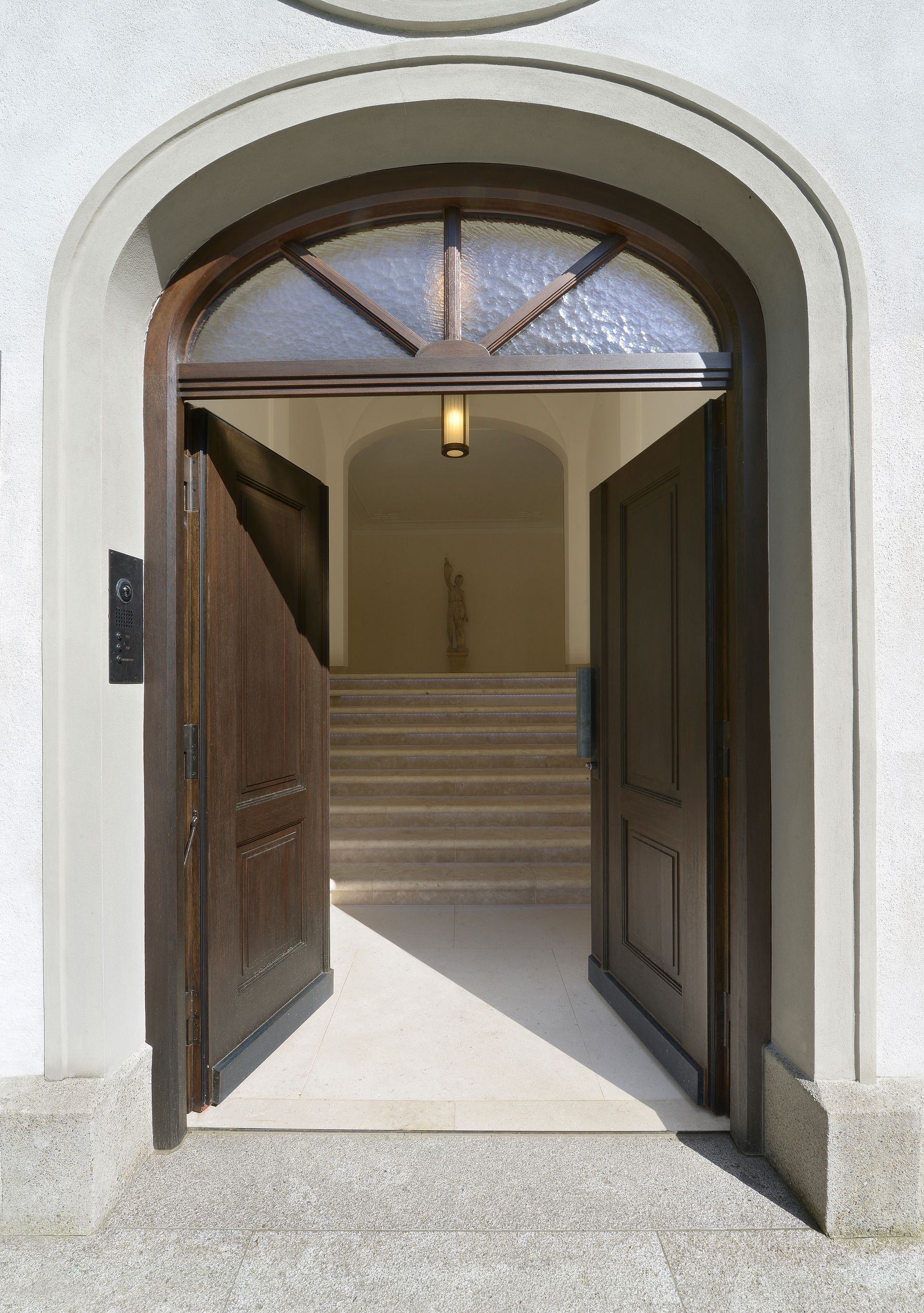 Open wooden doors in a white arched doorway, leading to a hallway with stairs.