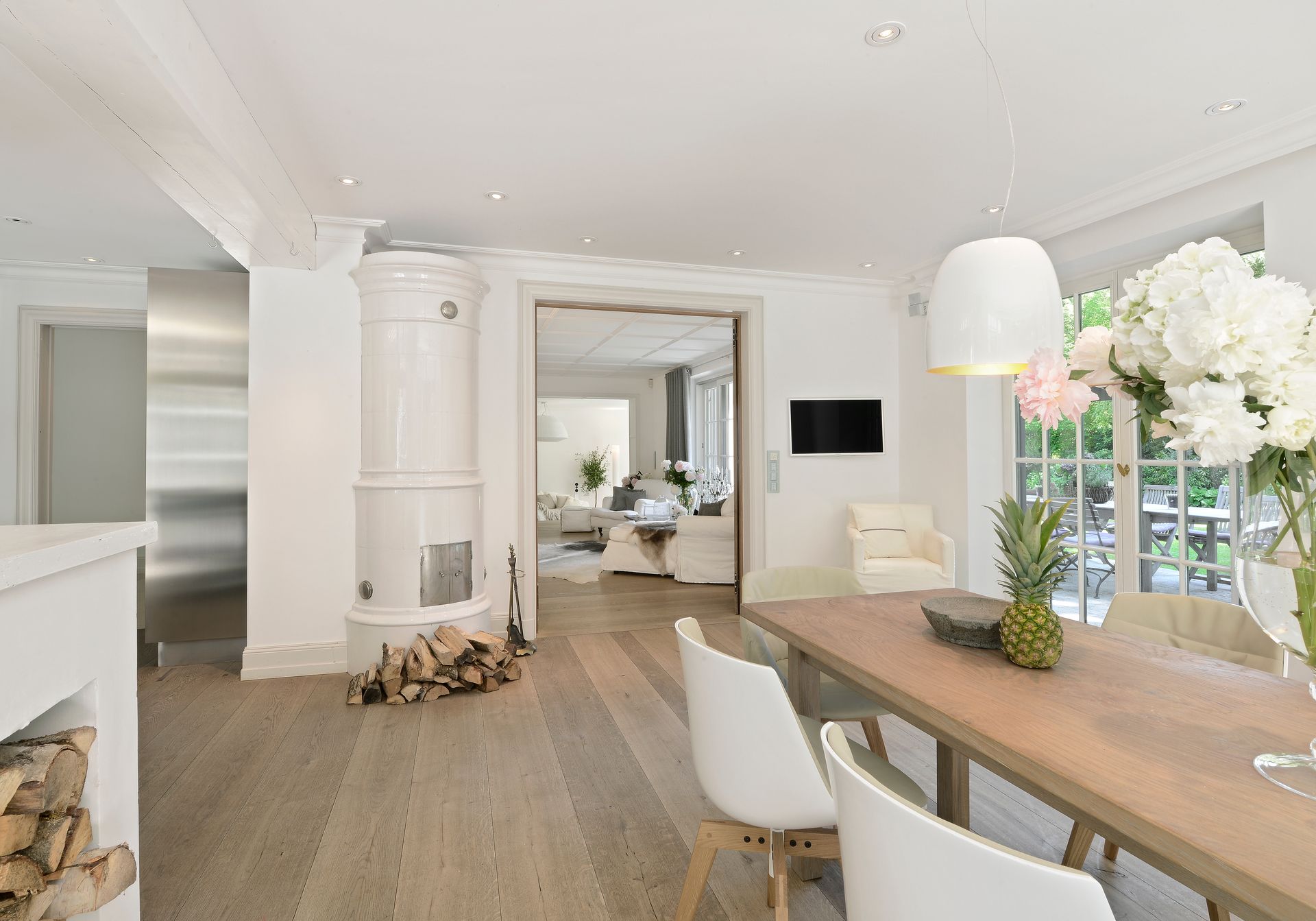 Spacious, bright dining room with wooden table, white chairs, and large window overlooking a garden.