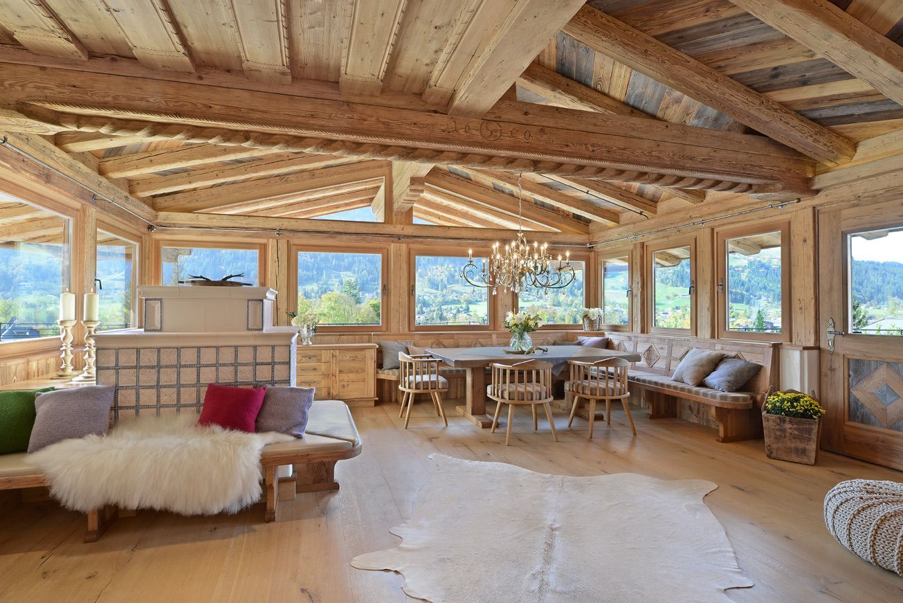 Wooden-paneled dining room with large windows, light wood furniture, a rustic bench, and a chandelier.