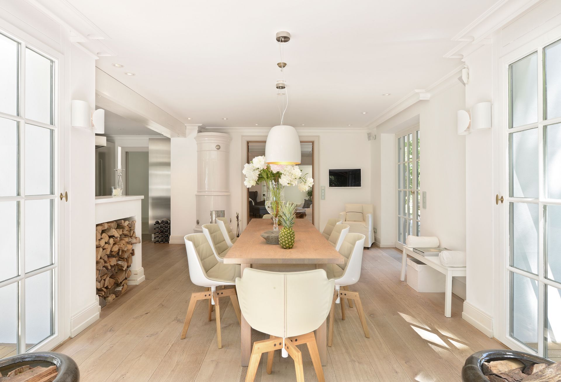 Bright dining room with a long wooden table, white chairs, and large windows.