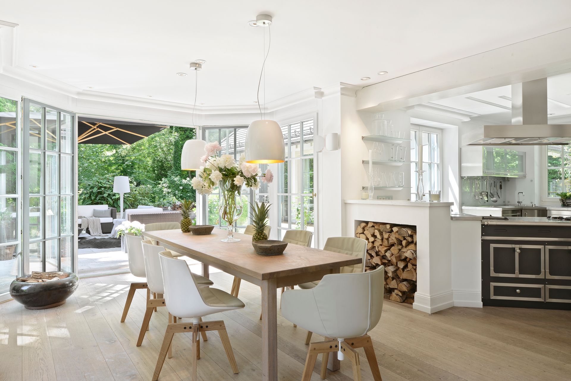 Bright, open dining room with long wooden table, white chairs, and glass doors opening to a garden.