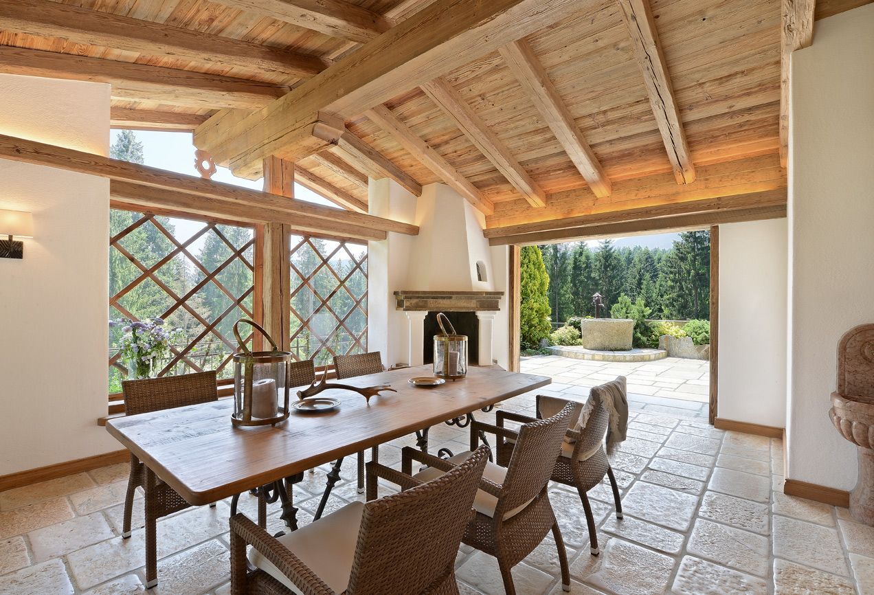 Dining room with wooden table, wicker chairs, fireplace, and mountain view through open doors.