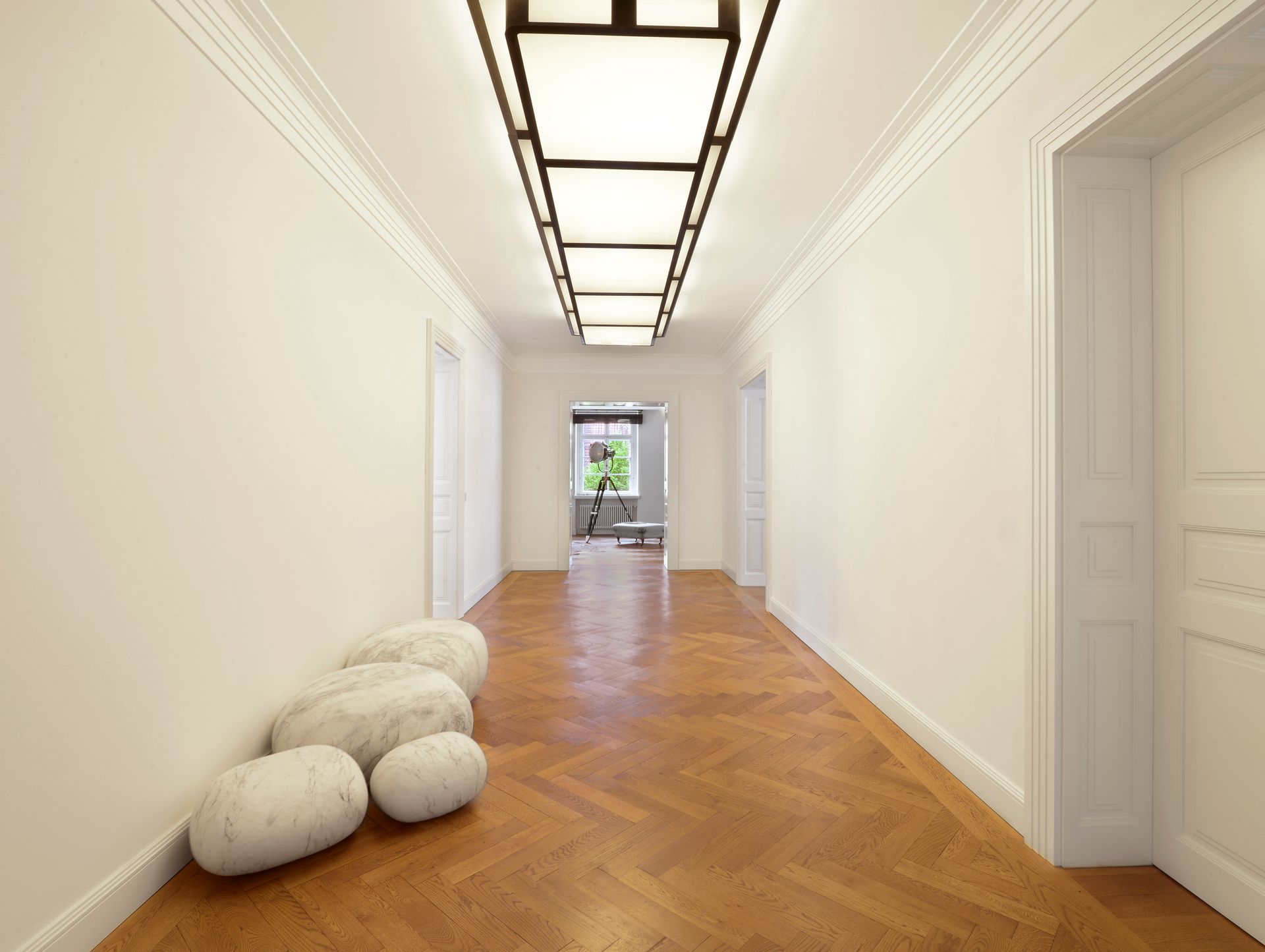 Long hallway with white walls, parquet floor, and modern overhead lighting.