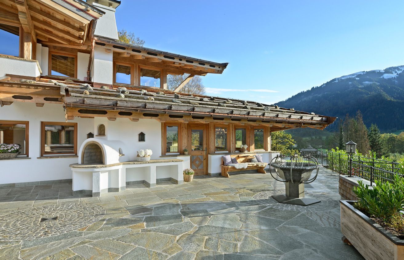 A scenic villa with a stone patio, outdoor kitchen, and mountain backdrop under a clear blue sky.