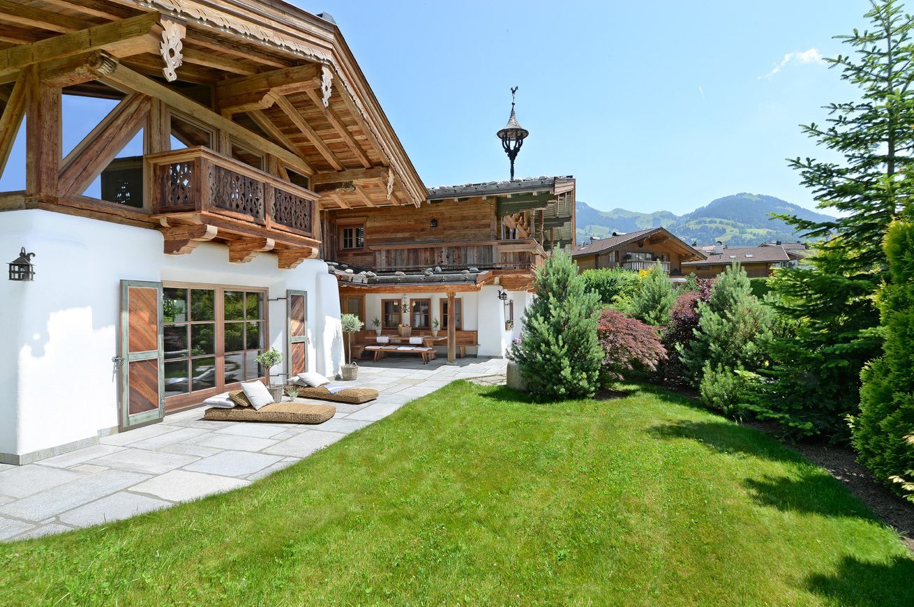 Exterior of a chalet-style building with a green lawn, patio, and surrounding trees under a blue sky.